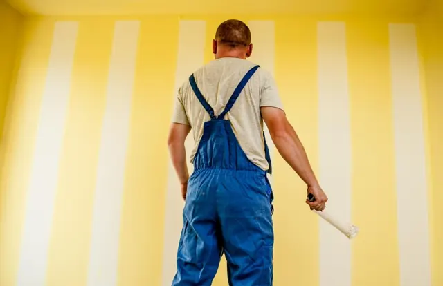 Painter with a roller in front of a freshly painted wall